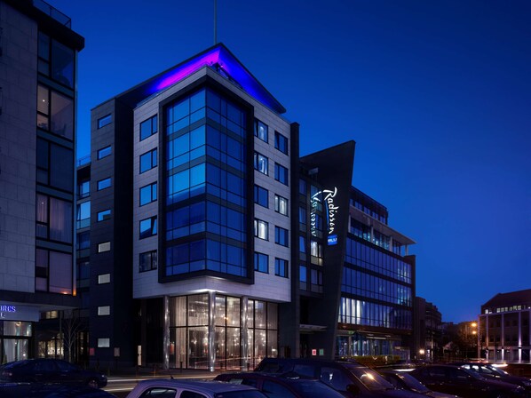 A modern hotel with a glass facade, a prominent neon sign, and a parking lot with cars. - Radisson Blu Royal Hotel, Dublin (Dublin)