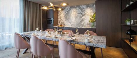 A modern dining area with a marble table, pink chairs, and a kitchen in the background.