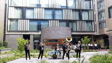 A group of musicians performing outdoors in front of a modern building with large windows and a courtyard.
