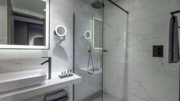 Un baño moderno con ducha de vidrio, un tocador blanco con grifo elegante y un espejo grande con iluminación integrada.