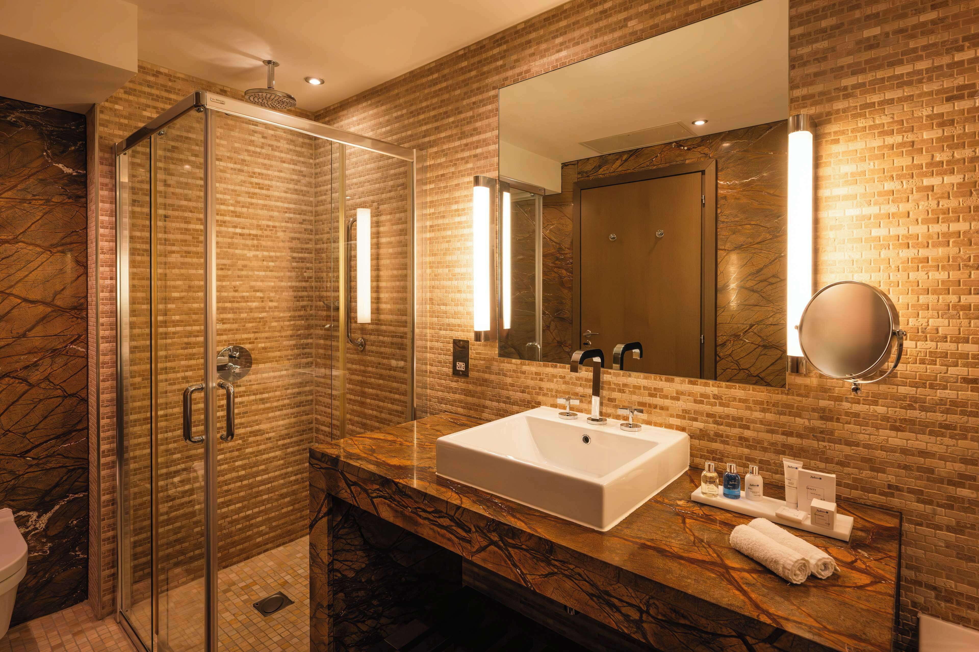 Un baño moderno con ducha envuelta en vidrio, un lavamanos grande y un espejo con iluminación integrada.