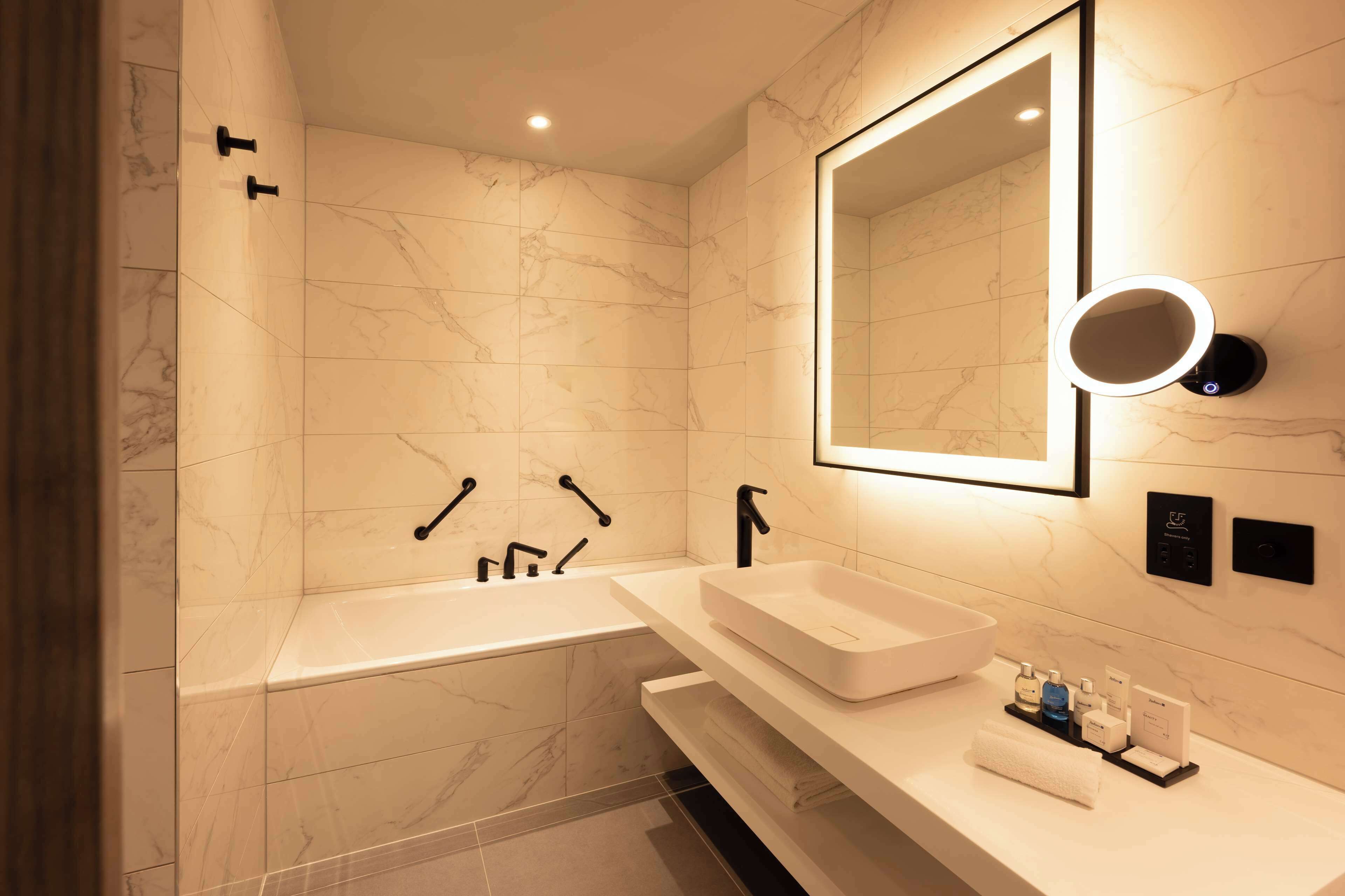 A modern bathroom with a large bathtub, a vanity with a sink, and a mirror with a light.