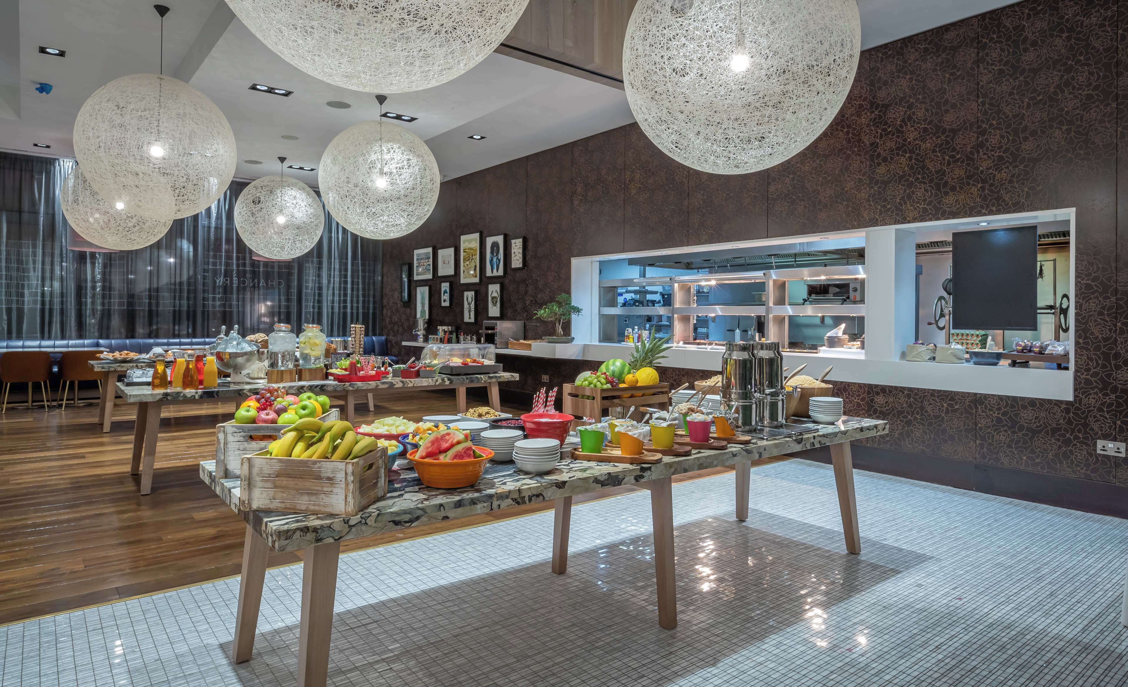 A modern dining area with a buffet setup, featuring a variety of fruits and beverages.