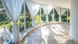 A modern interior with large windows, a curved staircase, and a view of a well-manicured garden. - Il San Francesco Charming Hotel (Sabaudia)