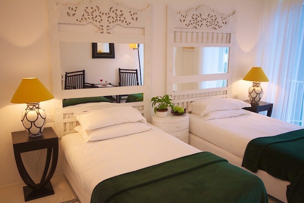 A hotel room with two beds, a mirror, a small table with a lamp, and a potted plant.