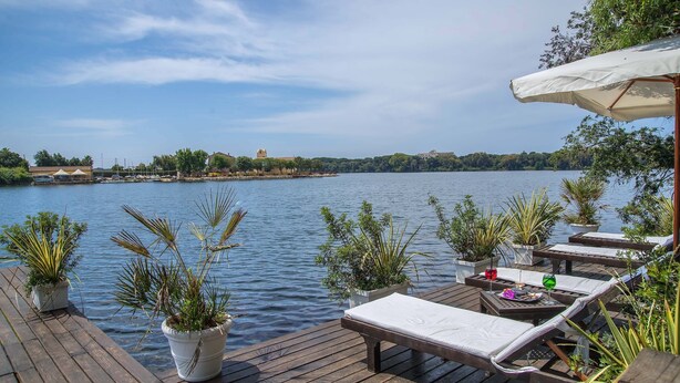 A wooden deck with lounge chairs and potted plants overlooking a calm lake. - Il San Francesco Charming Hotel (Sabaudia)