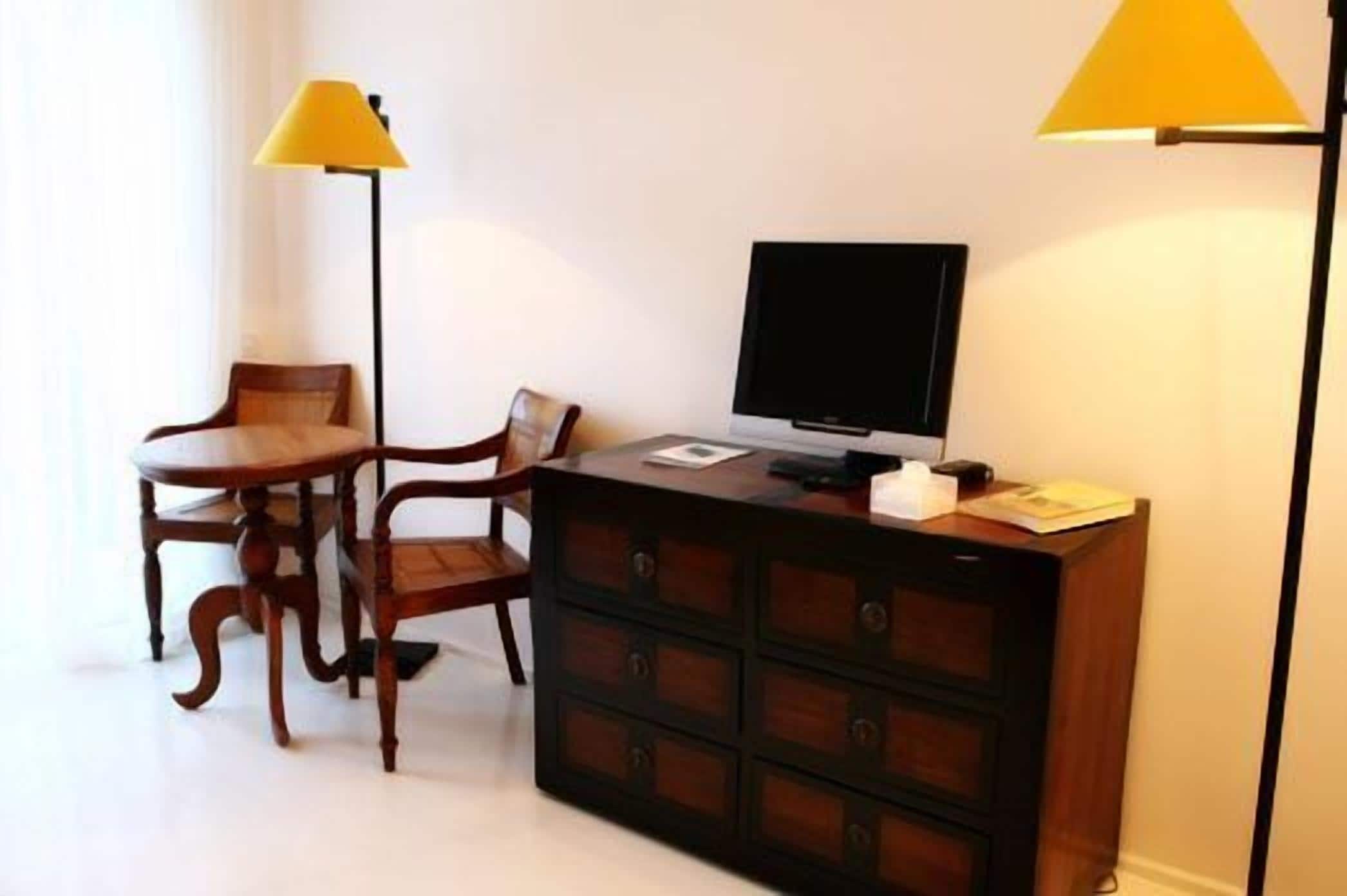 Ein Hotelzimmer mit Schreibtisch aus Holz, Fernseher, Lampe und Kommode.