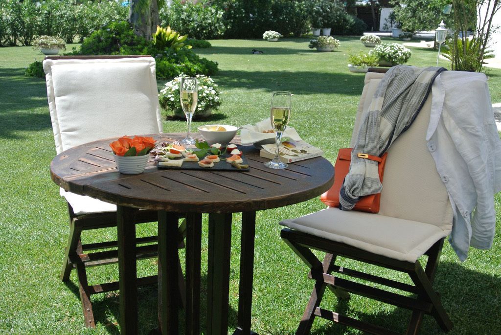 A round wooden table with a white bowl, two glasses of white wine, and a plate of food.