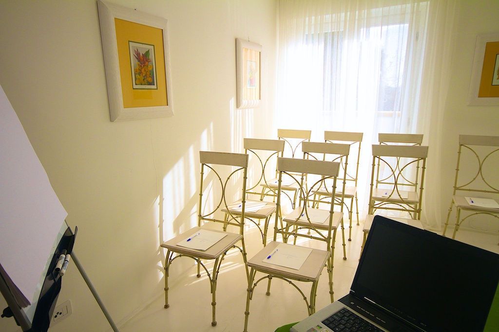Een kamer met een whiteboard, een laptop en meerdere stoelen rondom een tafel.