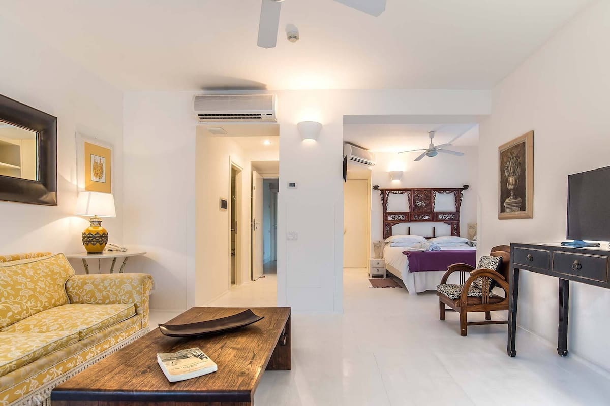 A hotel room with a sofa, a wooden coffee table, a TV, a bed with a headboard, and a desk.
