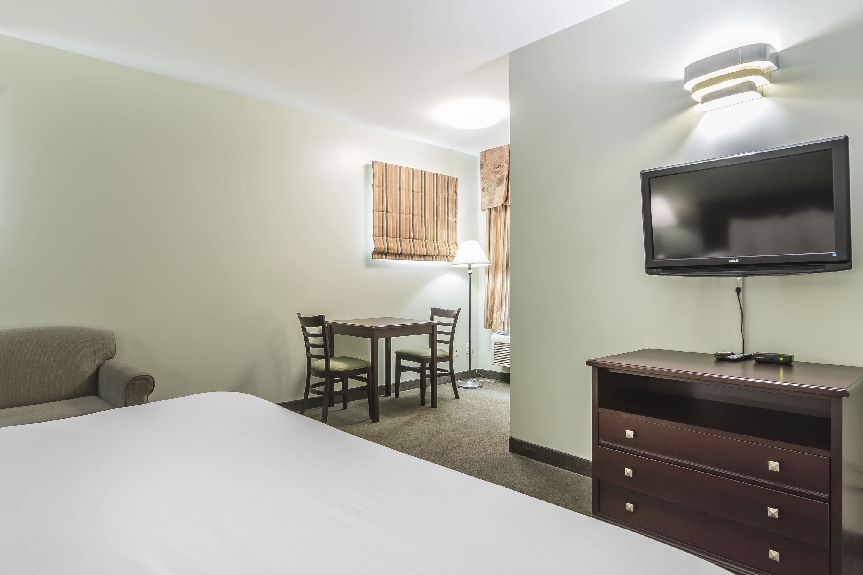 Ein Hotelzimmer mit einem Bett, einem Schreibtisch mit zwei Stühlen, einem Fernseher und einem Schminktisch.