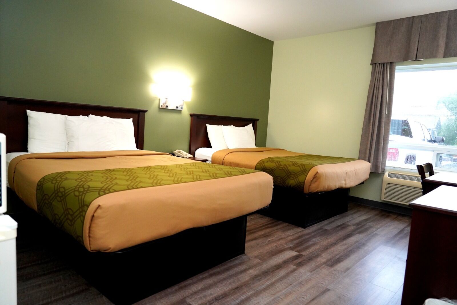 Habitación de hotel con dos camas, una mesita de noche, un escritorio y una ventana con cortinas.