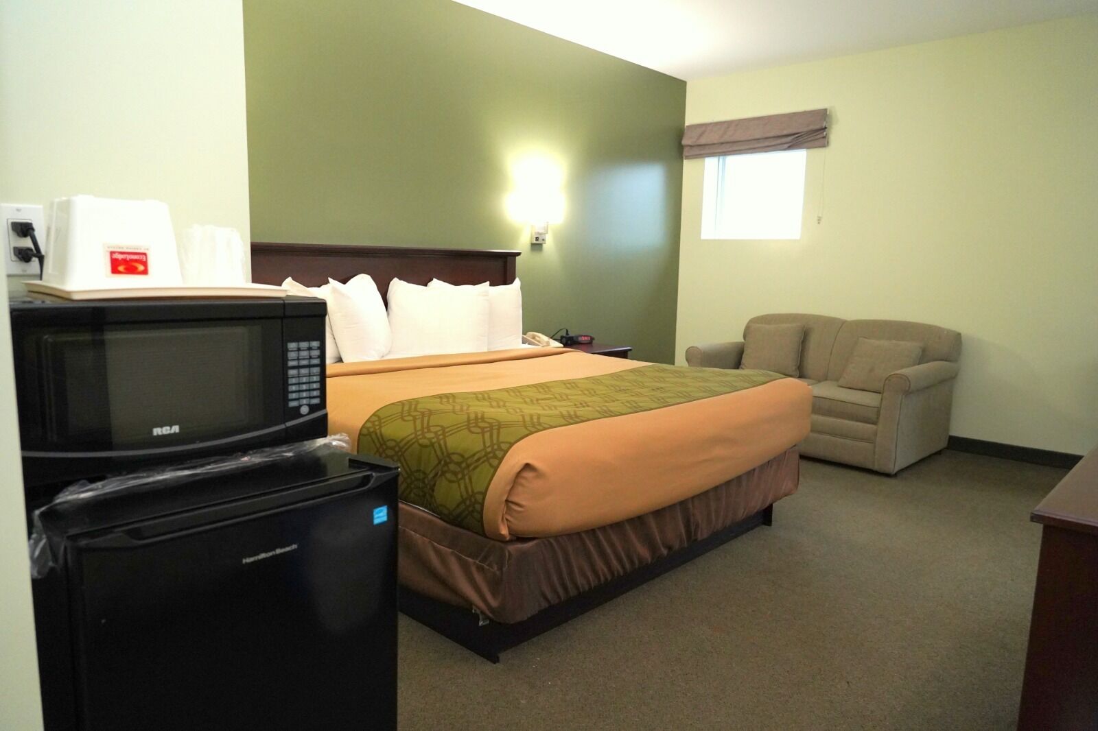 A hotel room with a bed, a chair, a microwave, and a refrigerator.