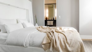 Un dormitorio moderno con una cama grande, un espejo y un baño pequeño visible al fondo.