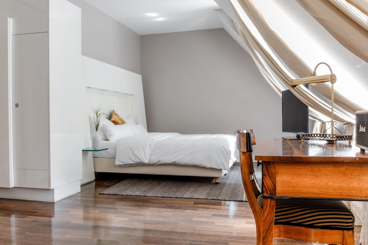 Un dormitorio moderno con cama, mesita de noche, lámpara y vistas a la ciudad.
