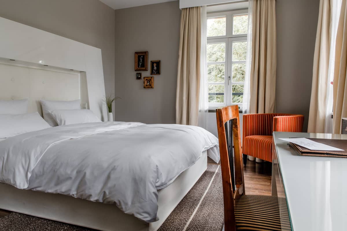 Una habitación de hotel con una cama grande, un escritorio con silla y una ventana con cortinas.