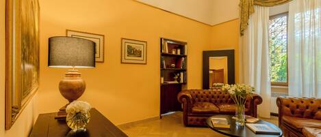 A living room with a wooden floor, a brown leather sofa, a round coffee table, a lamp, and a bookshelf.
