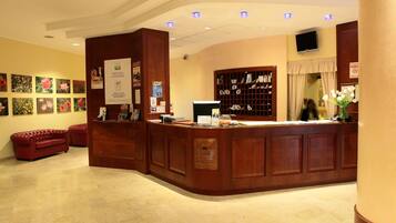 A hotel reception area with a wooden reception desk, a red leather sofa, and a wall with framed floral artwork.