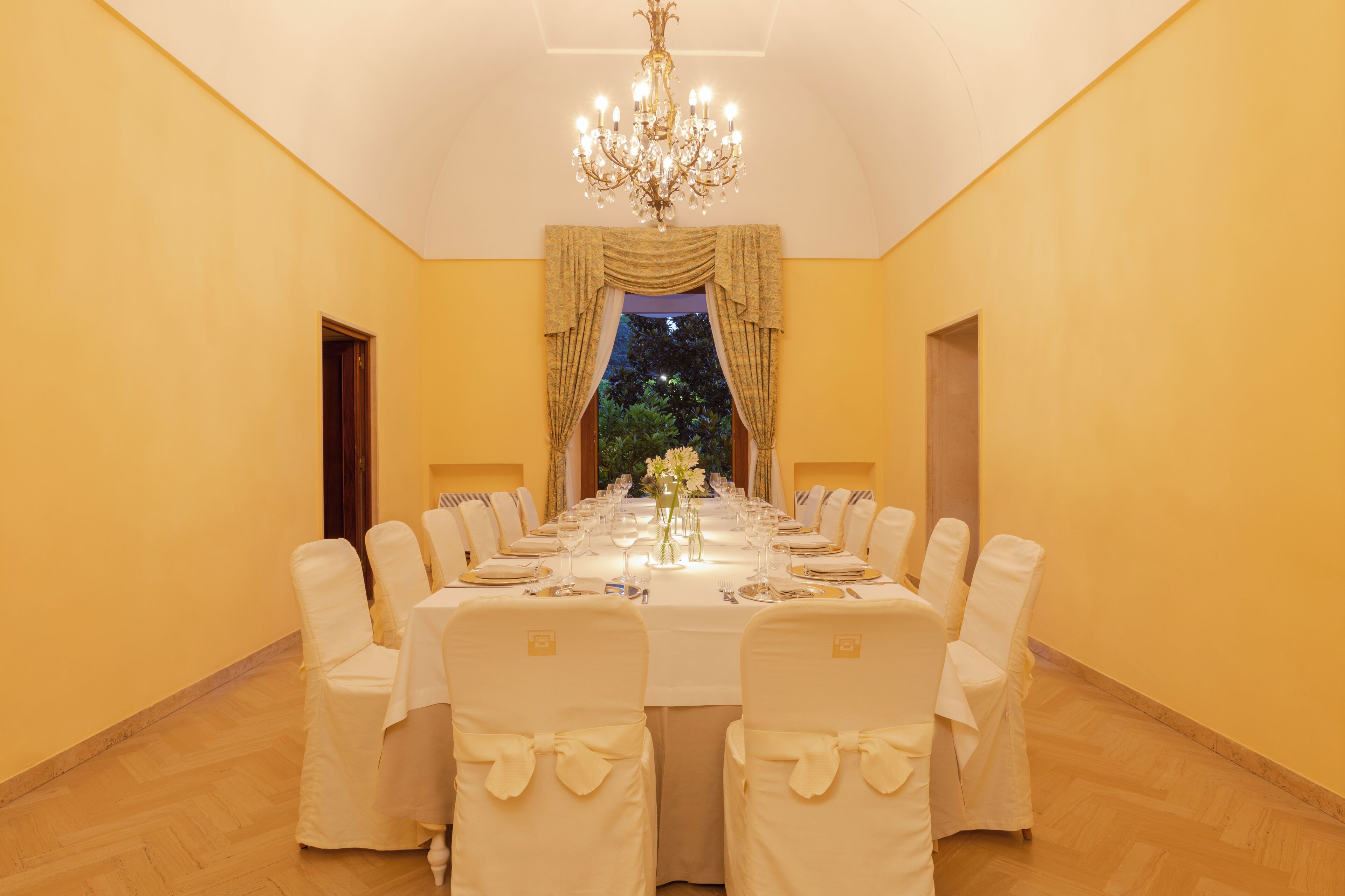 A formal dining room with a long table set for a meal, chairs with bow ties, and a chandelier.