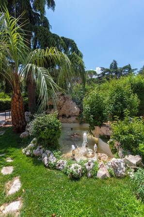 A garden with a palm tree, a small pond with a fountain, and various shrubs. - Park Hotel San Michele (Martina Franca)