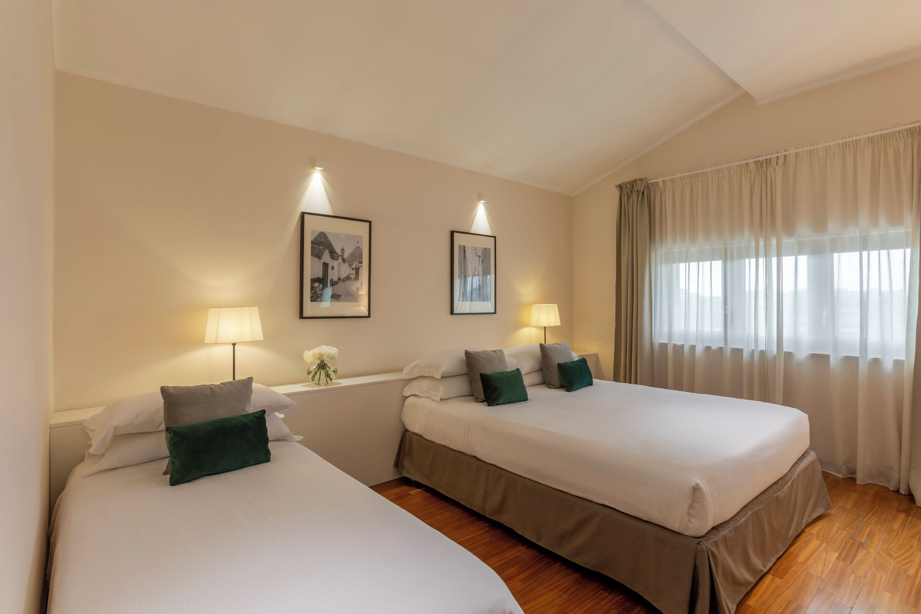 A hotel room with two beds, a window with curtains, and wall-mounted lamps.