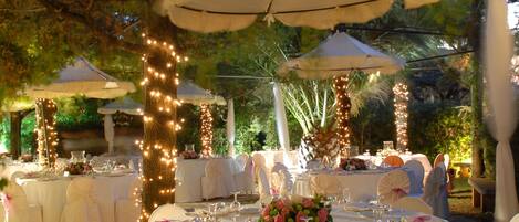 An outdoor wedding reception with round tables, white chairs, and string lights.