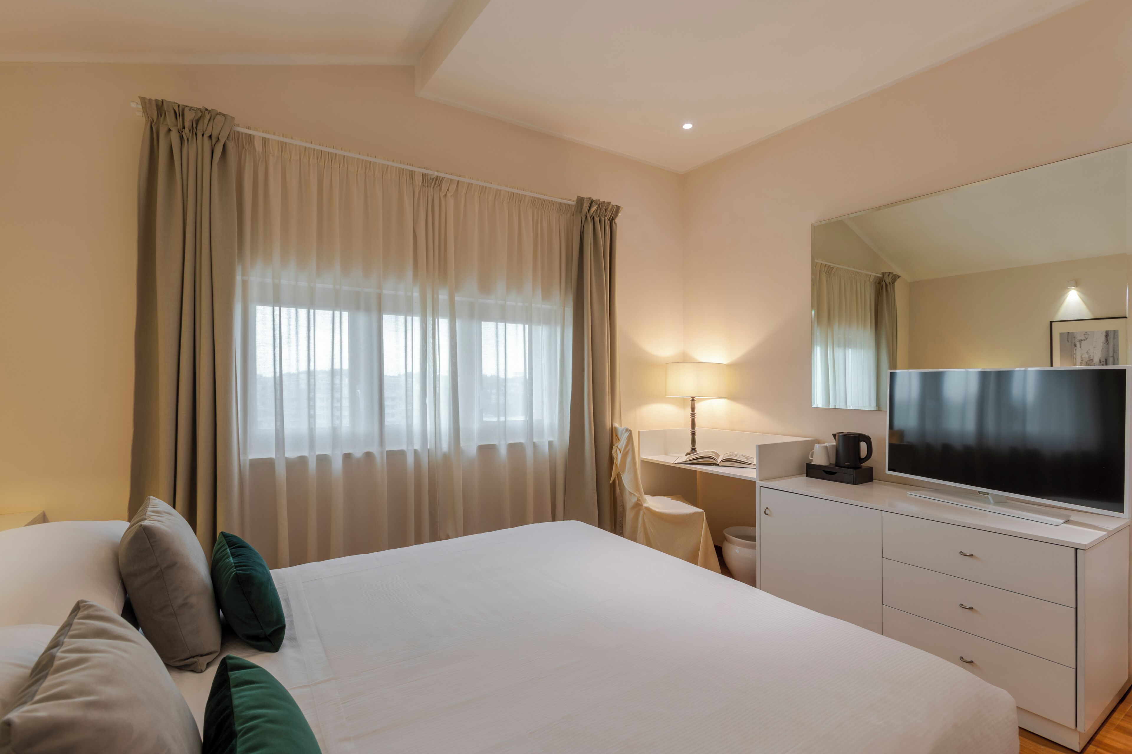 A hotel room with a bed, a desk, a television, and a window with curtains.