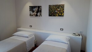 Una habitación con dos camas individuales, un cabecero blanco y dos cuadros colgados en la pared.