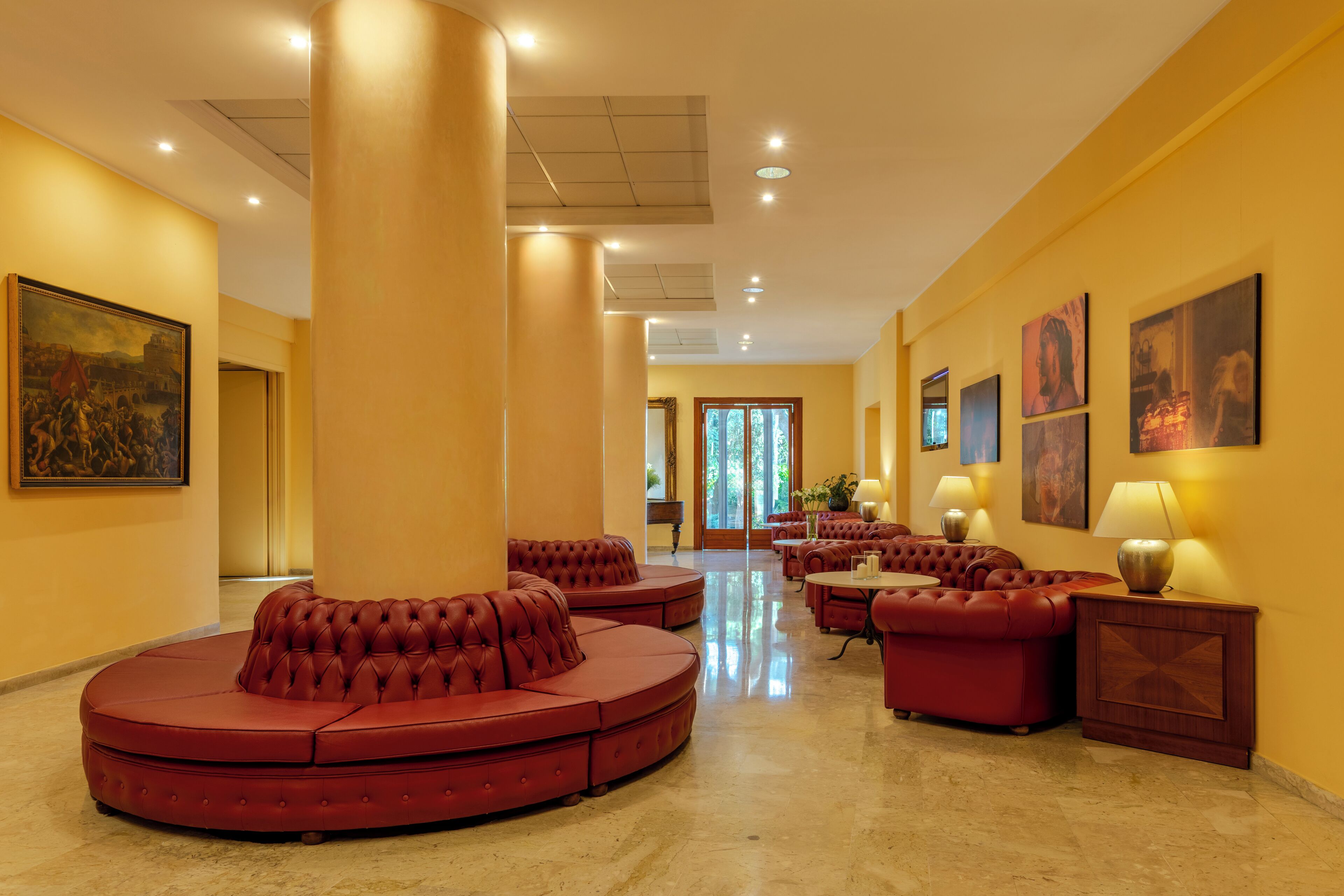 A spacious lobby with a red seating area, a large painting on the left, and several wall-mounted lamps.