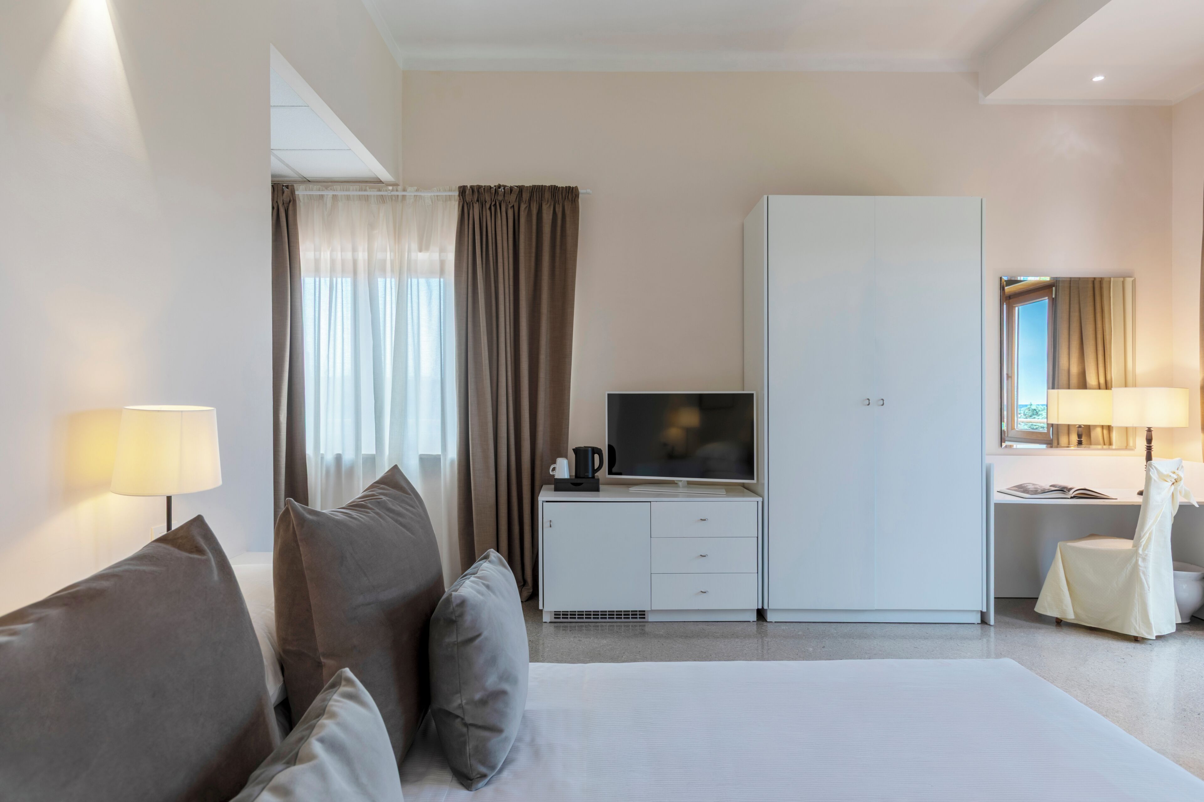 Une chambre d’hôtel comprenant un lit, un téléviseur posé sur un meuble, un bureau avec une chaise et une armoire.