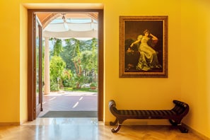 A room with a bench, a framed painting, and a view of a garden through an open doorway. - Park Hotel San Michele (Martina Franca)