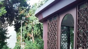 Een gebouw met een brede, gewelfde entree, decoratieve metalen poorten en een betegeld terras met een potplant en een grote vaas.