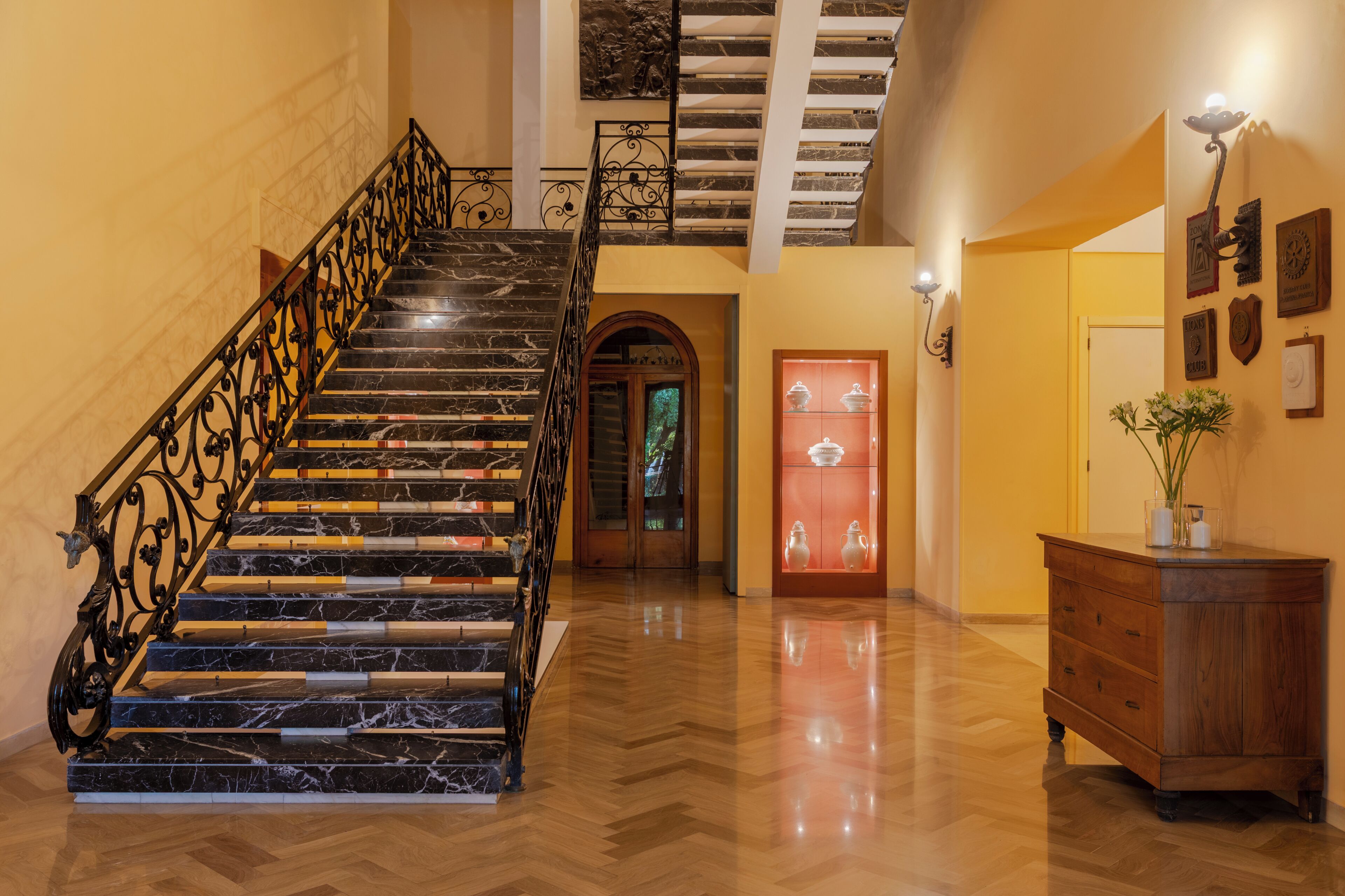 A grand staircase with marble steps and ornate metal railings, leading to a second-floor landing with a view of the outdoors.