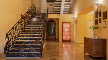A grand staircase with marble steps and ornate metal railings, leading to a second-floor landing with a view of the outdoors.