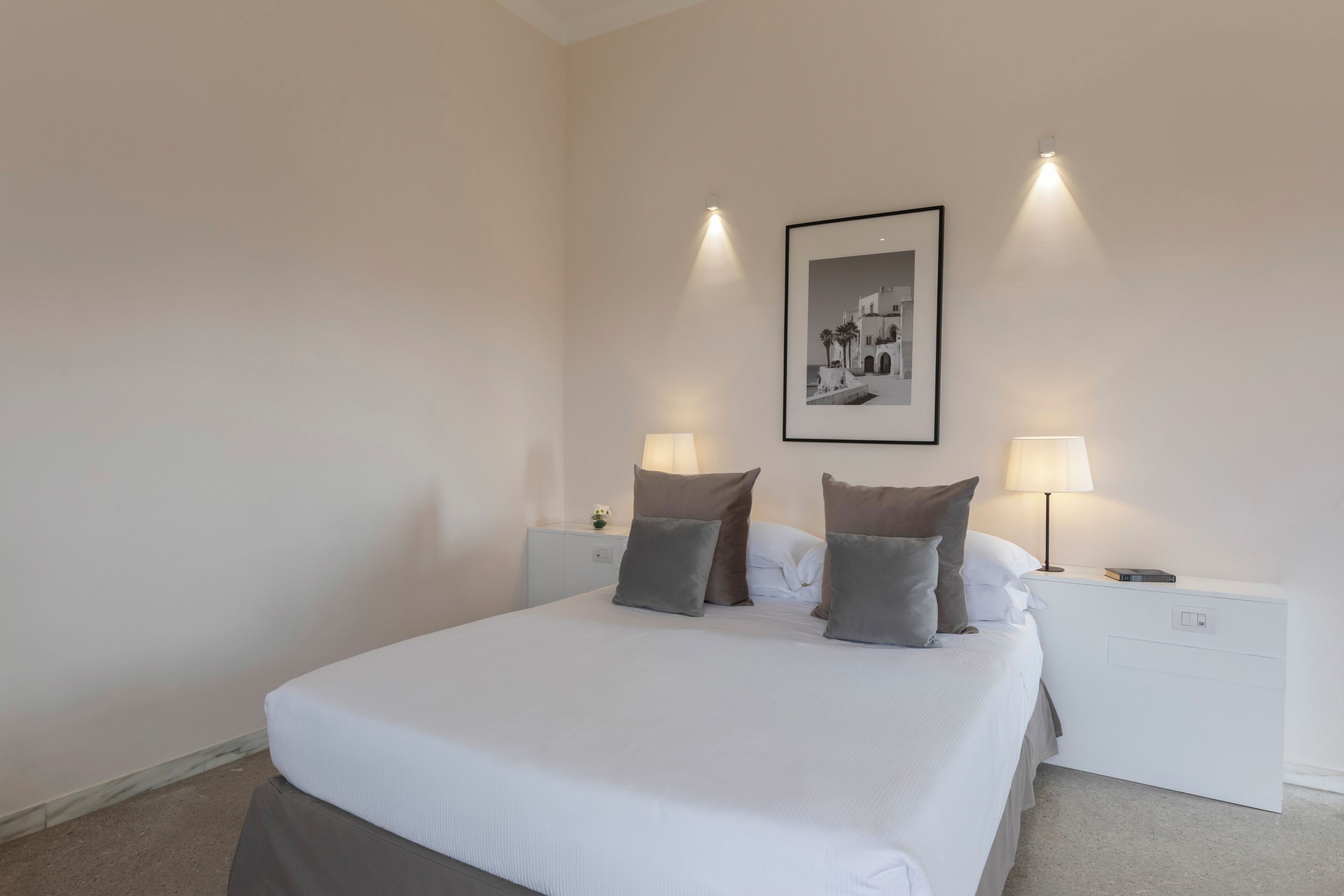 A hotel room with a large bed, two bedside tables with lamps, a framed picture on the wall, and a small plant on one table.