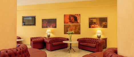 A hotel room with a yellow wall, two red leather sofas, a small round table, and three wall-mounted paintings.