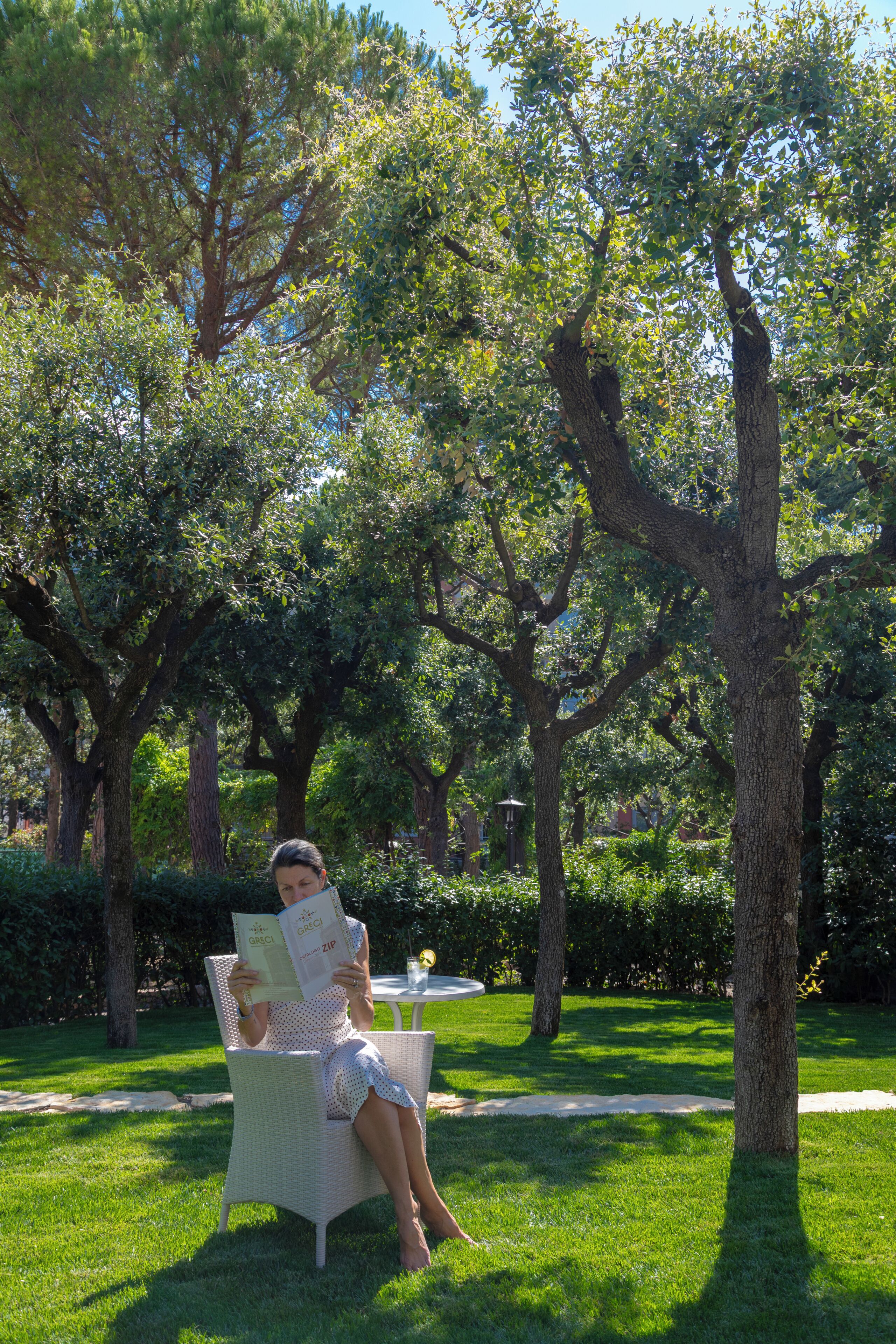 Una mujer sentada en una silla de mimbre en un parque, leyendo un libro.