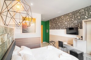 A modern hotel room with a large bed, a desk, a TV, and a geometric light fixture.