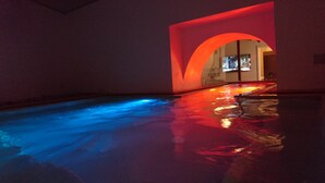 An indoor swimming pool with blue and red lighting, surrounded by walls and a glass window. - Hotel Centrale (Syracuse)