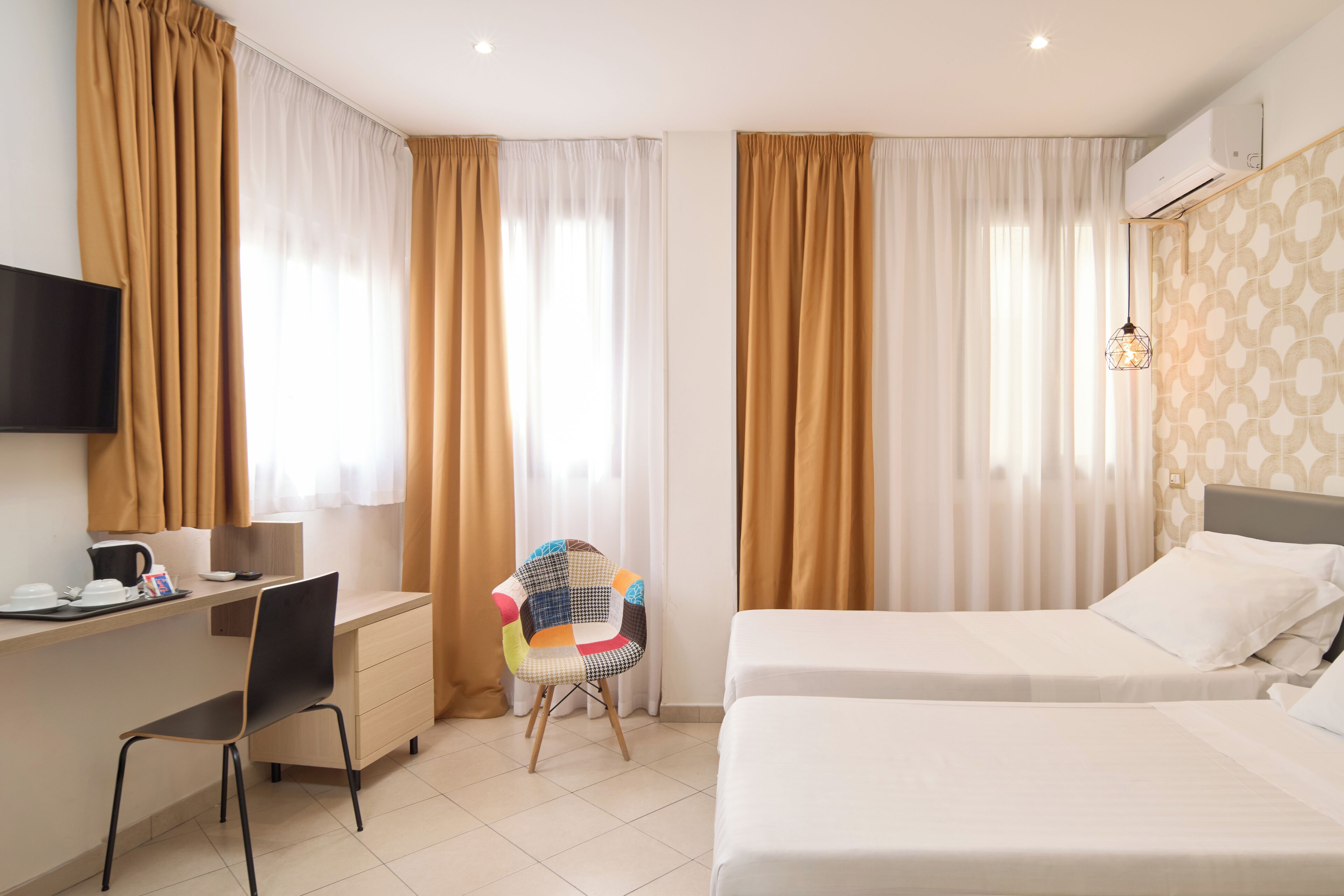 Una habitación de hotel con dos camas, un escritorio con una silla, un televisor y cortinas.