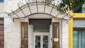 A hotel entrance with a metal archway, double doors, and two potted plants. - Hotel Centrale (Syracuse)