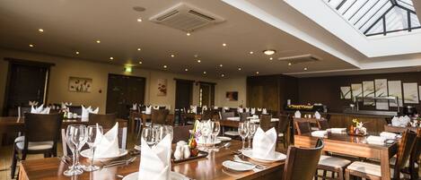 A spacious dining area with multiple tables set for service, a skylight above, and a clean, modern interior.