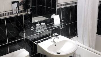 Un baño con un lavamanos blanco, azulejos de mármol negro, un inodoro blanco y un espejo sobre el lavamanos.