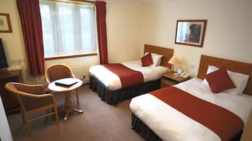 Habitación de hotel con dos camas, una silla, una mesita, una lámpara y una ventana con cortinas.