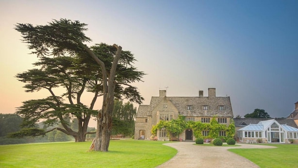 A large stone building with a traditional design, a well-maintained lawn, and a prominent tree in the foreground. - Stanton House Hotel (Swindon)
