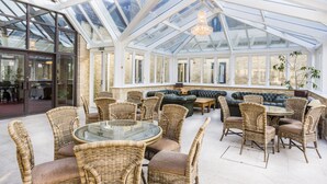 A conservatory with wicker furniture, a glass table, and a chandelier. - Stanton House Hotel (Swindon)
