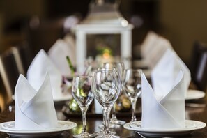 A dining table set with white napkins folded into cones, clear wine glasses, and plates. - Stanton House Hotel (Swindon)