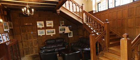 A lobby with a wooden staircase, leather sofas, and framed pictures on the walls.
