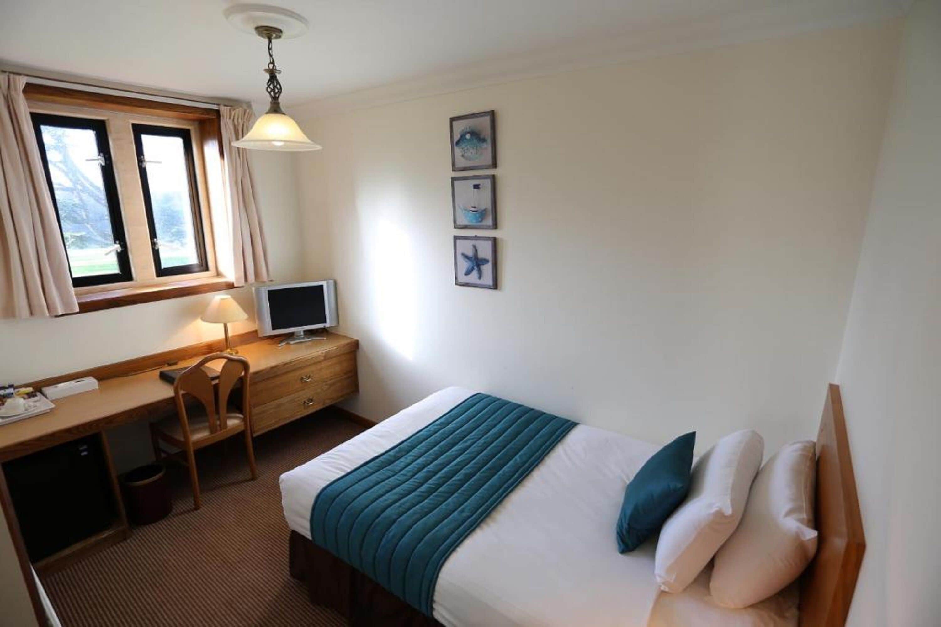 Una habitación de hotel con cama, escritorio, silla y televisor.