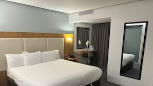 A hotel room with a large bed, a desk with a chair, a mirror, and a bathroom visible through an open door. - Stanton House Hotel (Swindon)